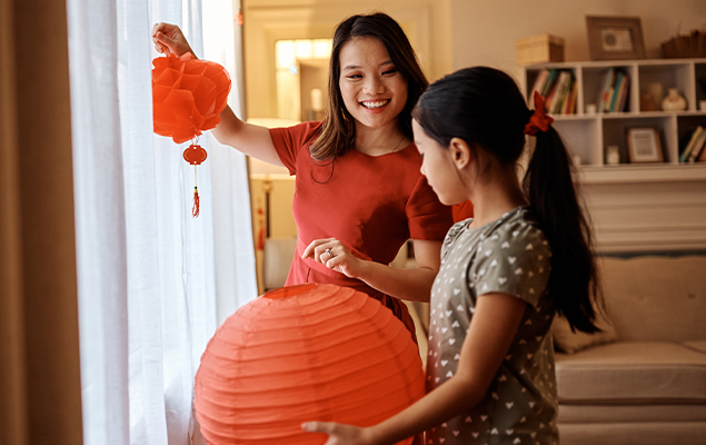 Woman and daughter hanging paper lanterns in their living room