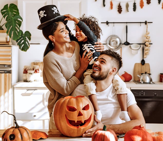 family with young child posing with a carved pumpkin and playing around with hats