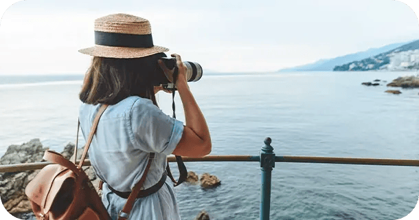 an image of a woman on a seaside overlook taking a picture with a professional camera