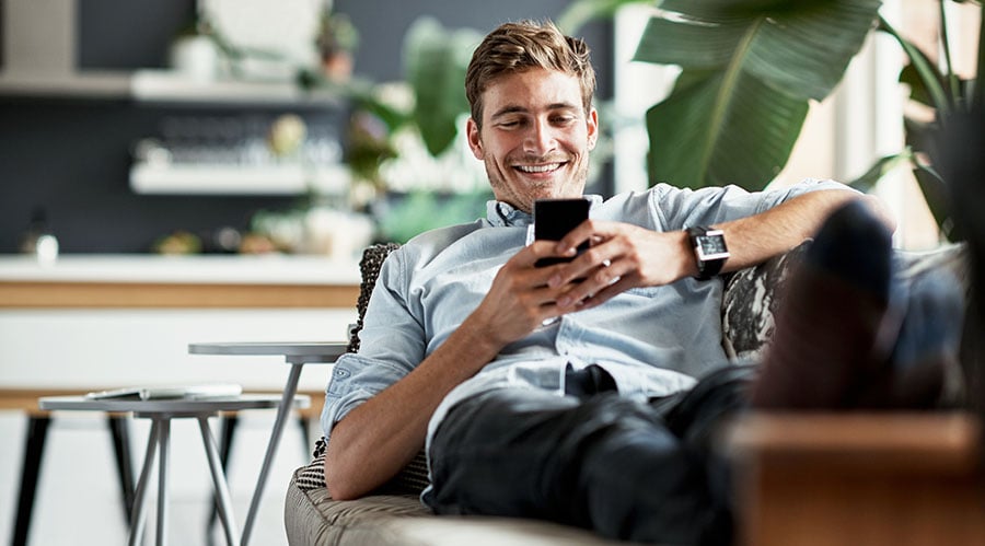 a man relaxing on a couch while looking at a smartphone