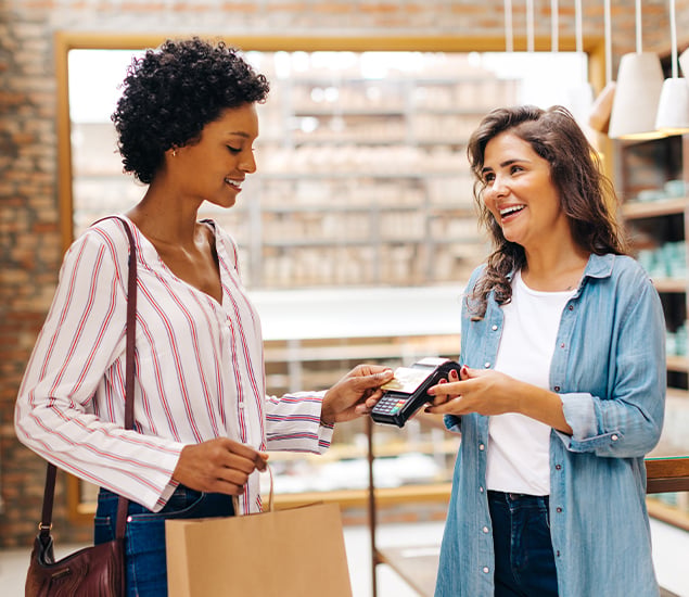 Two women in a retail store as one woman uses a card reader to make a purchase
